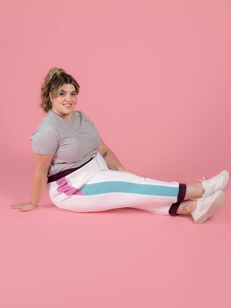 Plus size model is sitting down wearing Cece joggers sewing pattern from Tilly and the Buttons in white with colour block side panel and pockets