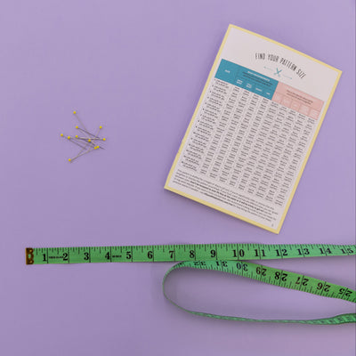 Measurement chart, green measuring tape, and pins on a purple background