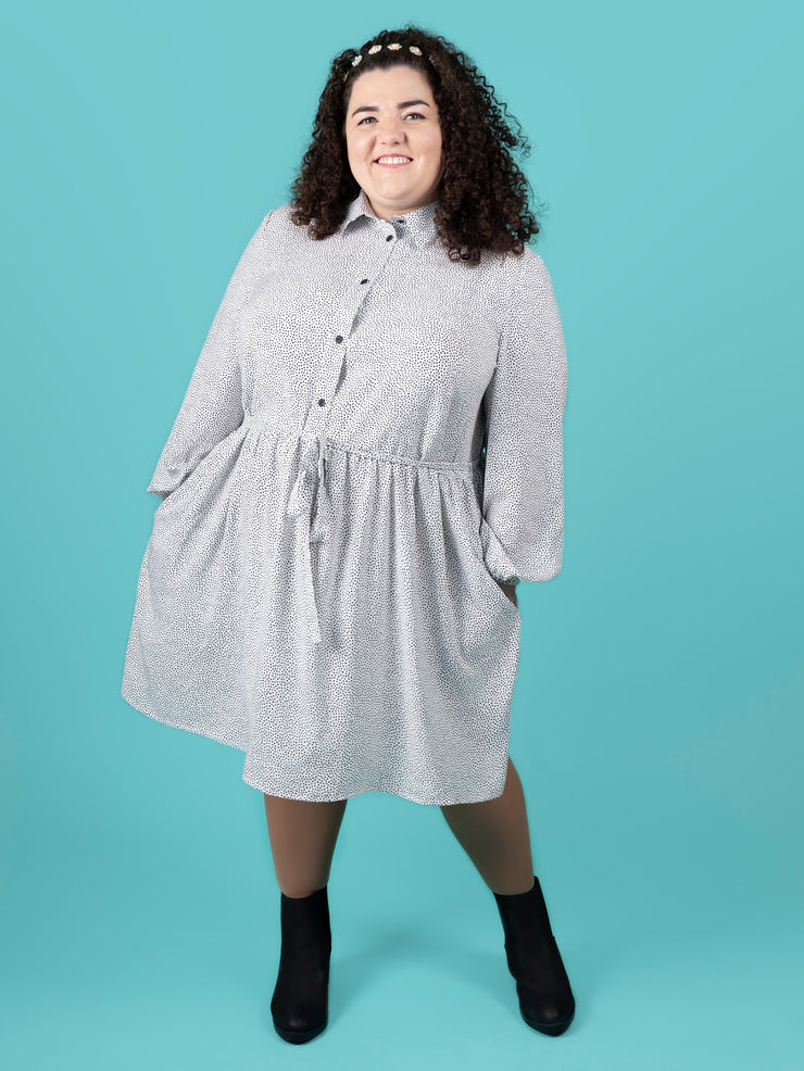Woman wearing a white and black polka dot Lyra dress against a teal background
