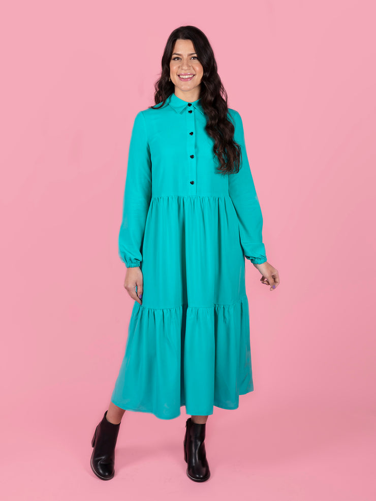 Woman wearing a teal Lyra dress against a pink background