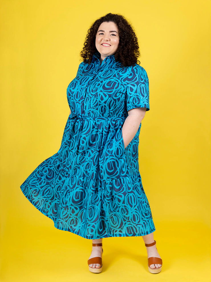 Woman wearing a blue patterned Lyra dress against a yellow background