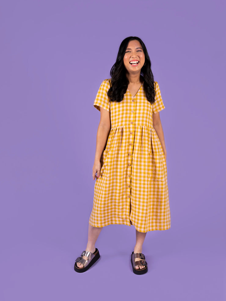 Woman wearing a yellow gingham Nell dress on a purple background
