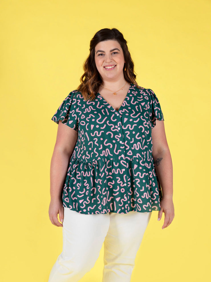 Woman wearing a green and pink patterned Nell blouse against a yellow background