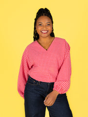 Woman wearing a pink checkered Samara top and dark jeans against a yellow background