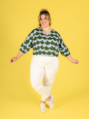 Model wearing a green and white patterned Samara top with white jeans on a yellow background
