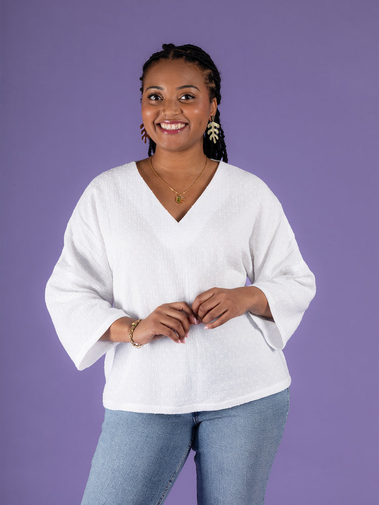 Model wearing a white Samara top and blue jeans against a purple background