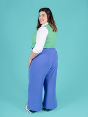 Woman wearing a green top, white shirt, and blue Thea trousers against a blue background