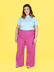 Woman wearing a light blue top and pink Thea trousers on a yellow background