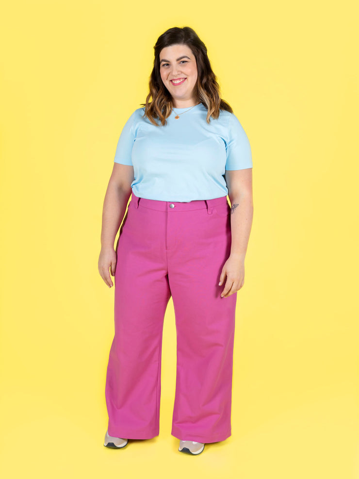 Woman wearing a light blue top and pink Thea trousers on a yellow background
