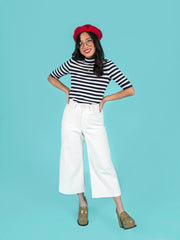 Woman wearing a black and white striped top, white Thea trousers, and a red beret on a blue background