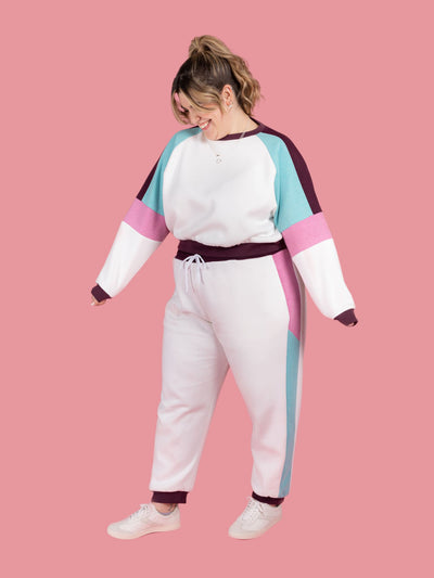 Model wearing a Drew sweatshirt and Cece joggers matching tracksuit set. Sewn in colour-blocked in white, blue, pink and purple. 