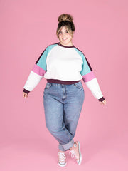 Person wearing a colorful sweater and jeans on a pink background