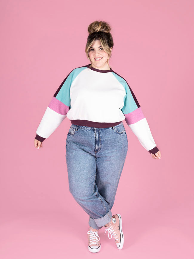 Person wearing a colorful sweater and jeans on a pink background