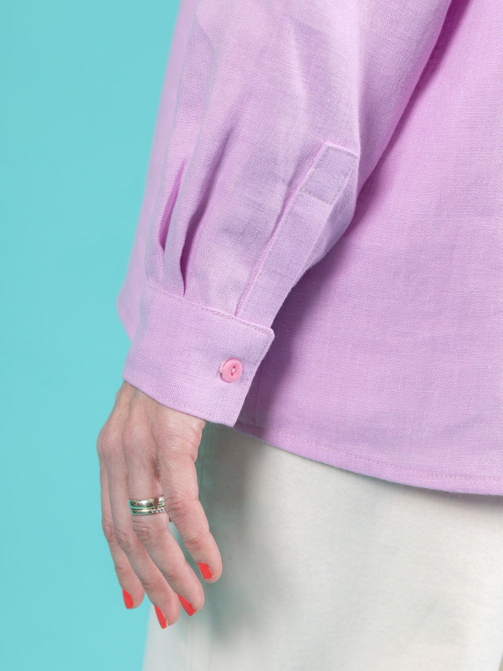 Close up of the cuff on a lilac long sleeve Frida shirt against a teal background.