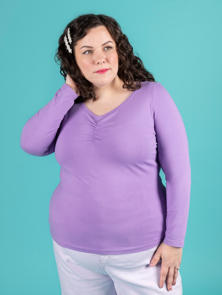 Model with brunette curly hair wears purple long sleeve jersey top with sweetheart neckline