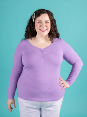 Model with brunette curly hair wears purple long sleeve jersey top with sweetheart neckline