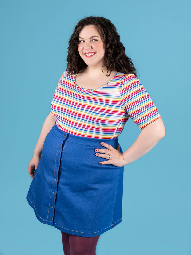 Model with curly brunette hair wears short sleeve rainbow stripe Agnes top