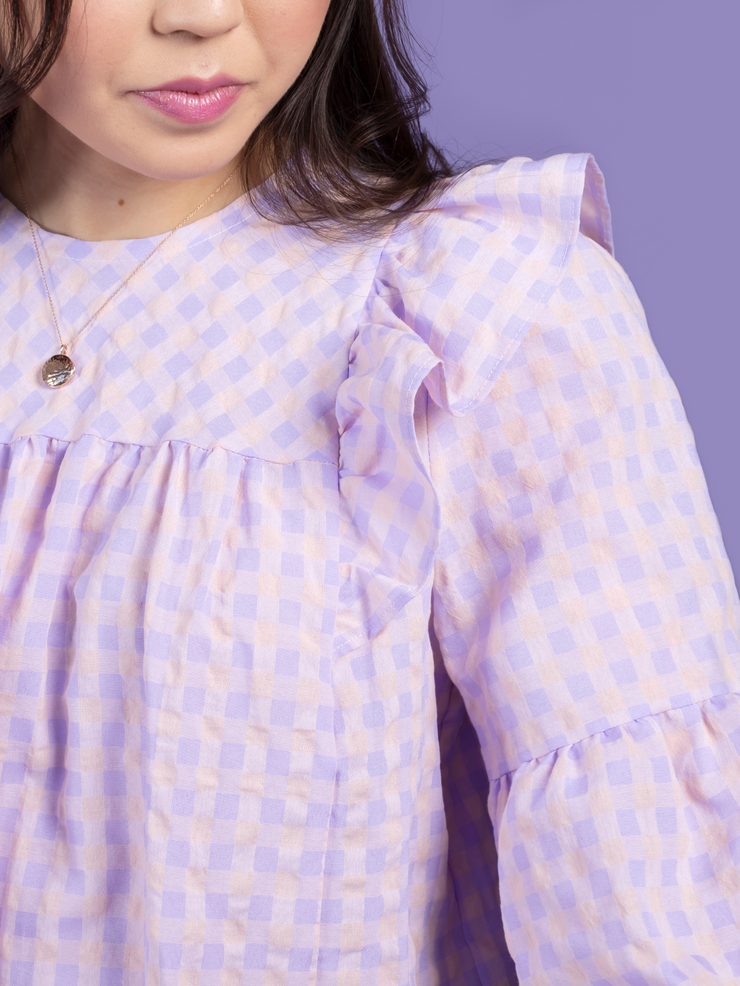 Close up of model wearing a lilac and pink gingham blouse, made using the Marnie sewing pattern in cotton.